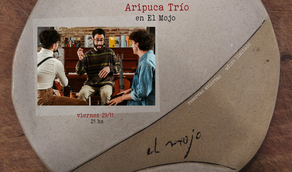 Afiche de recital con una imagen de 3 músicos sentados en círculo en un ensayo, más atrás hay una guitarra y un piano que tiene algunos libros arriba. Afiche de recital con una imagen de 3 músicos sentados en círculo en un ensayo, más atrás hay una guitarra y un piano que tiene algunos libros arriba.